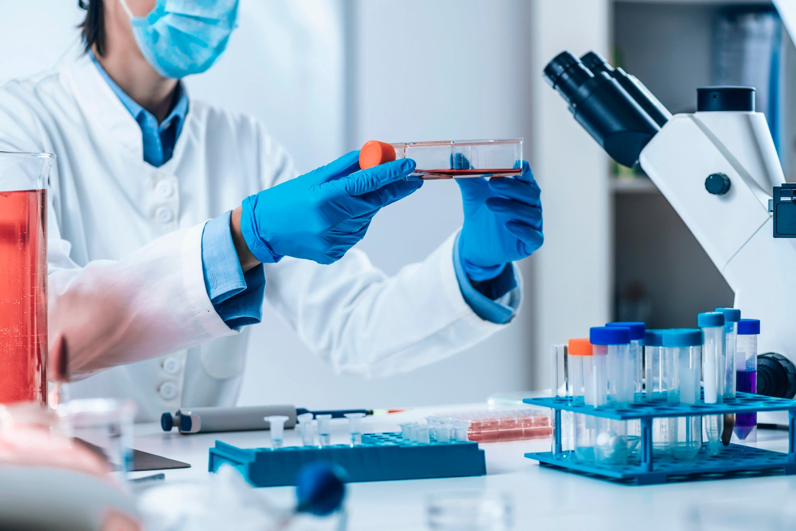 Scientist in lab gear pouring liquid into a test tube under purple lighting Scientist analyzing cultured mammalian cells under the microscope